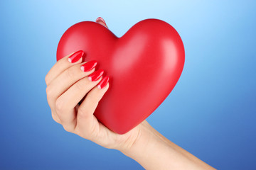 Red heart in woman's hand on color background