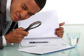 Man examining a document with a magnifying glass - obrazy, fototapety, plakaty