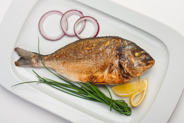 grilled fish on a plate with onions and lemon