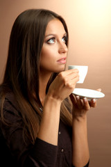 beautiful young woman with cup of coffee, on brown background