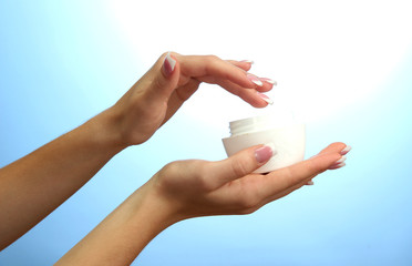 Beautiful woman hands with cream, on blue background