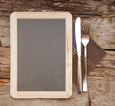 Menu blackboard lying on old  wooden table with knife and fork