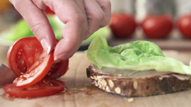 Female hand slicing and putting tomato on slice of bread