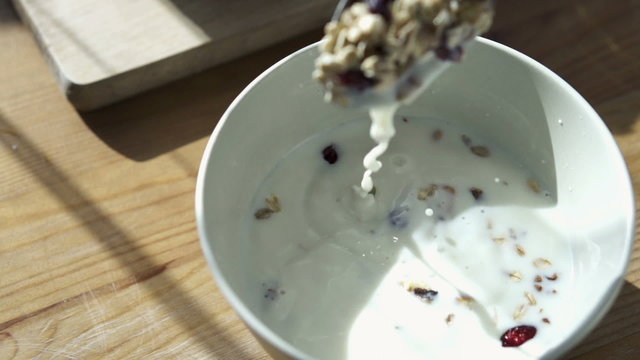 Spoon mixing muesli and milk in bowl, slow motion shot at 240fps