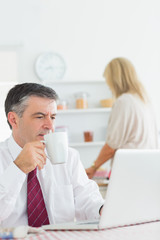 Man drinking coffee while checking laptop