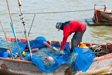 Fisherman mending net in his boat