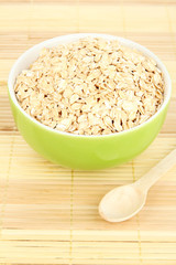 Green bowl full of oat flakes with wooden spoon