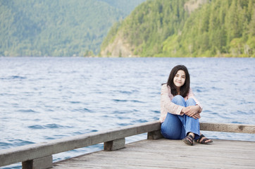 Fototapeta na wymiar Young teen girl sitting quietly on lake pier, relaxing