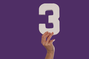 Female hand holding up the number 3 from the bottom