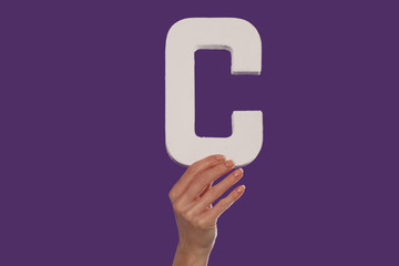 Female hand holding up the letter C from the bottom