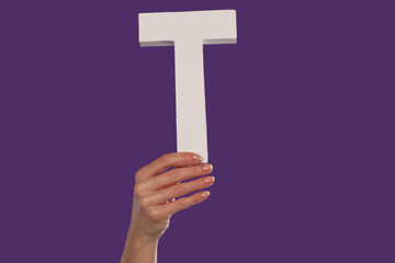 Female hand holding up the letter T from the bottom