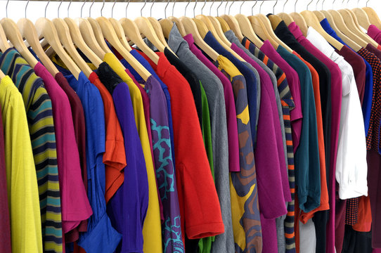 Variety of casual clothes of different colors on wooden hangers