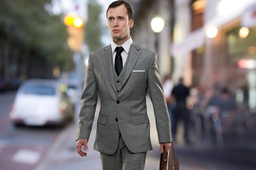 Man in classic grey suit with briefcase walking outdoors