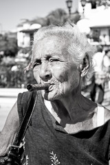 Old wrinkled woman with red flower smoking cigar.  Cuba
