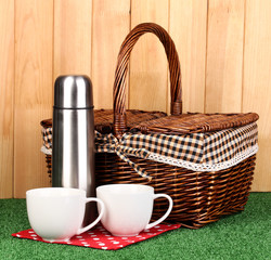 metal thermos with cups and basket on grass on wooden