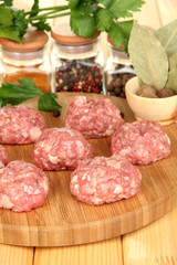 Raw meatballs with spices on wooden table