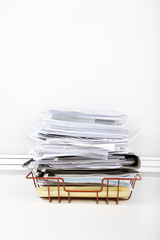 Documents overflowing in desk tray against white wall