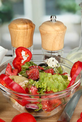 Fresh greek salad in glass bowl surrounded by ingredients for