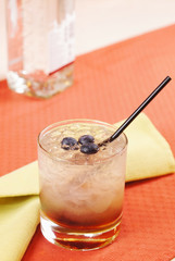 Bramble cocktail in a glass with blueberry and a bottle of gin