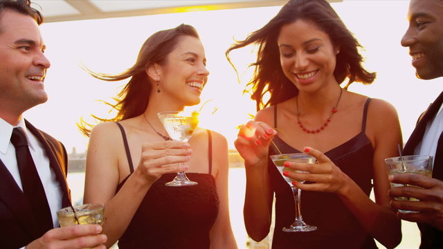 Two women drinking cocktails with men at luxury sunset party dressed in black 