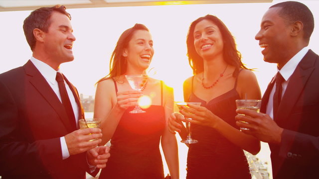 Multi ethnic friends drinking cocktails dressed in black at sunset roof party 