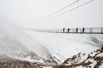 A bridge for hikers in snowy Austrian Alps during a foggy day