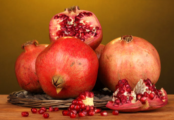Ripe pomegranates on wicker cradle on yellow background