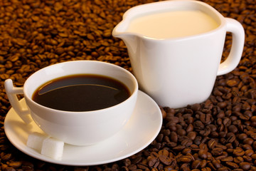 A cup of strong coffee and sweet cream on coffee beans close-up