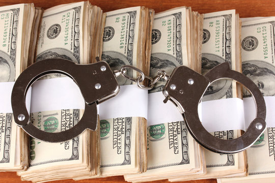 Handcuffs on the packs of dollars on wooden table close-up