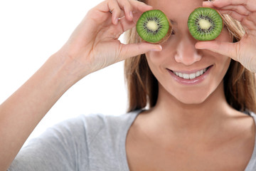 Woman covering her eyes with slices of kiwi