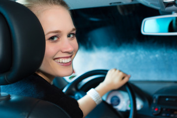 Young woman drives car in wash station