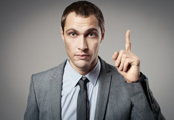 Young businessman criticizing on gray background