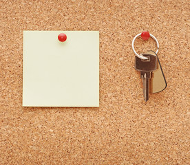 clean post-it note and home keys stuck to a cork notice board