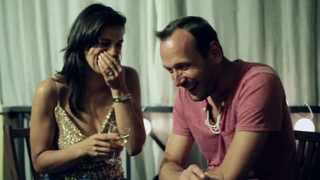 Laughing couple with wine on balcony at night 