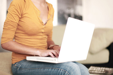 Naklejka premium Junge Frau sitzt auf der Couch und arbeitet am Laptop