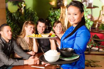 Young people with waitress eating in Thai restaurant