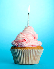 tasty birthday cupcake with candle, on blue background