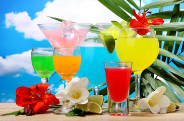 exotic cocktails and flowers on table on blue sky background