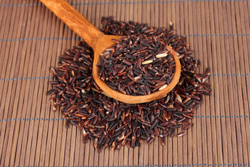black rice  in wooden  spoon on bamboo mat