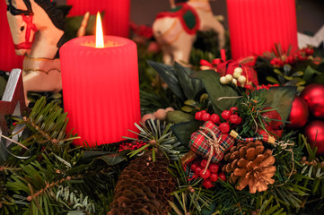 Adventsgesteck mit Christbaumschmuck und brennender Kerze