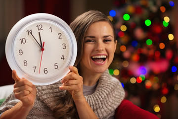 Happy woman showing clock in front of Christmas tree