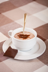 Mug with hot chocolate and a chocolate piece.