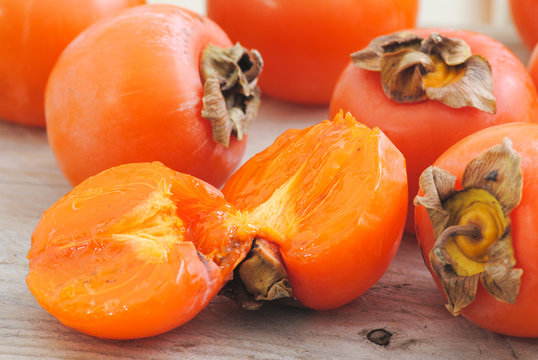 Close up fuyu persimmons fruits whole and cutted on white wood