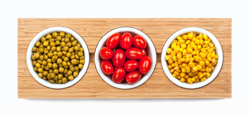 Corn, tomatoes and peas in white plates on wooden stand.