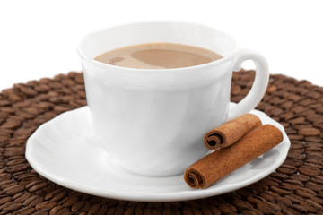 White cup of coffee with cinnamon, standing on coffee beans.