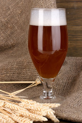 Glass of beer on wooden table on sacking background