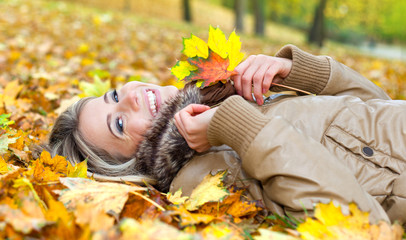 Young smiling woman lying on leaves in autumn