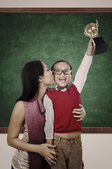 Boy raising trophy kiss by his mother in class