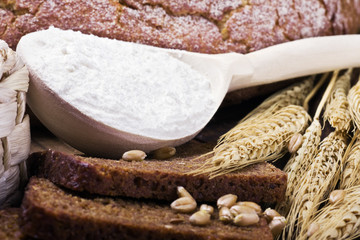 Wooden spoon with flour on background baked bread