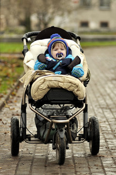 Serious baby in blue overalls sit in big three-wheeled buggy